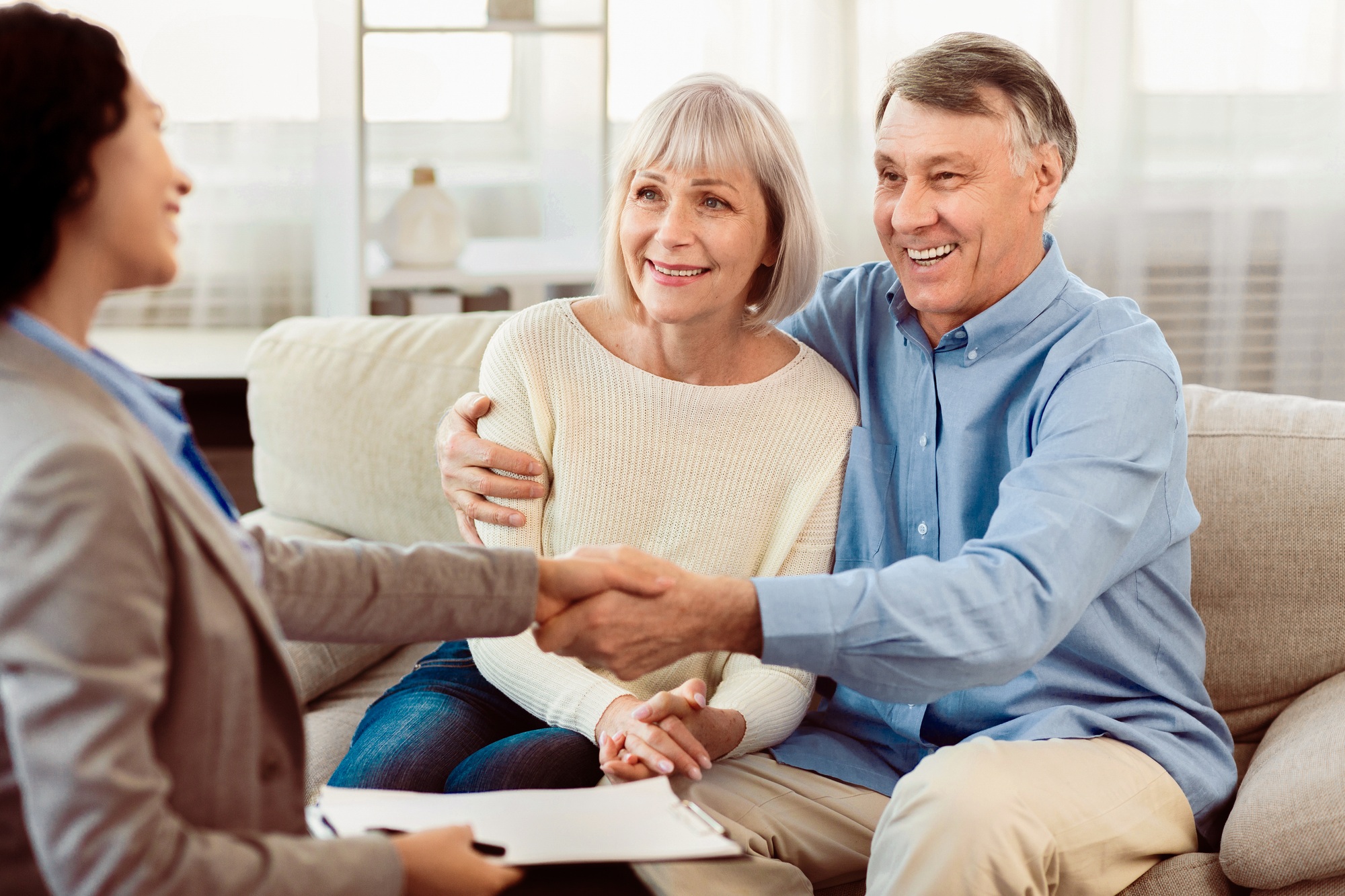 Female realtor handshaking happy mature couple at home